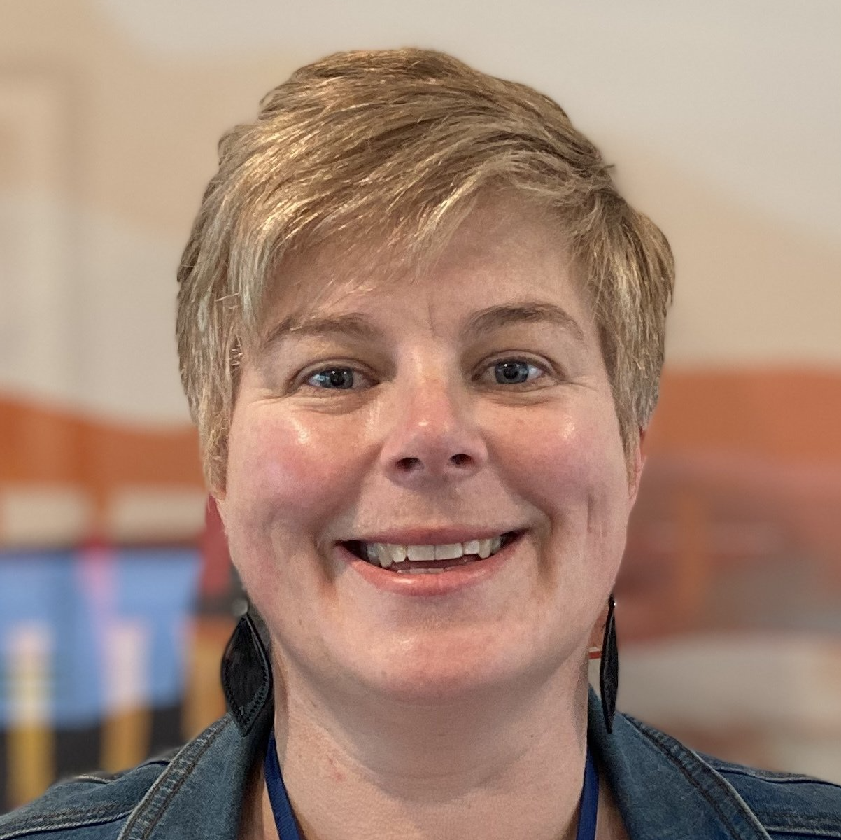 A close up of a woman 's face smiling and wearing a denim jacket.