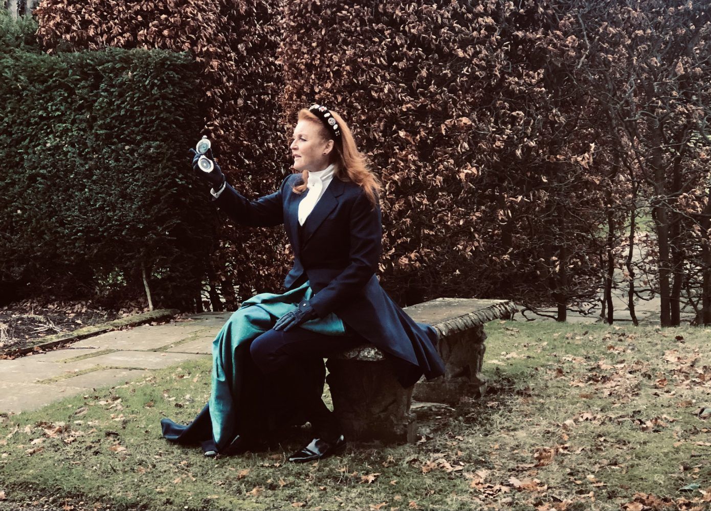 A woman is sitting on a bench in a park holding a glass of water