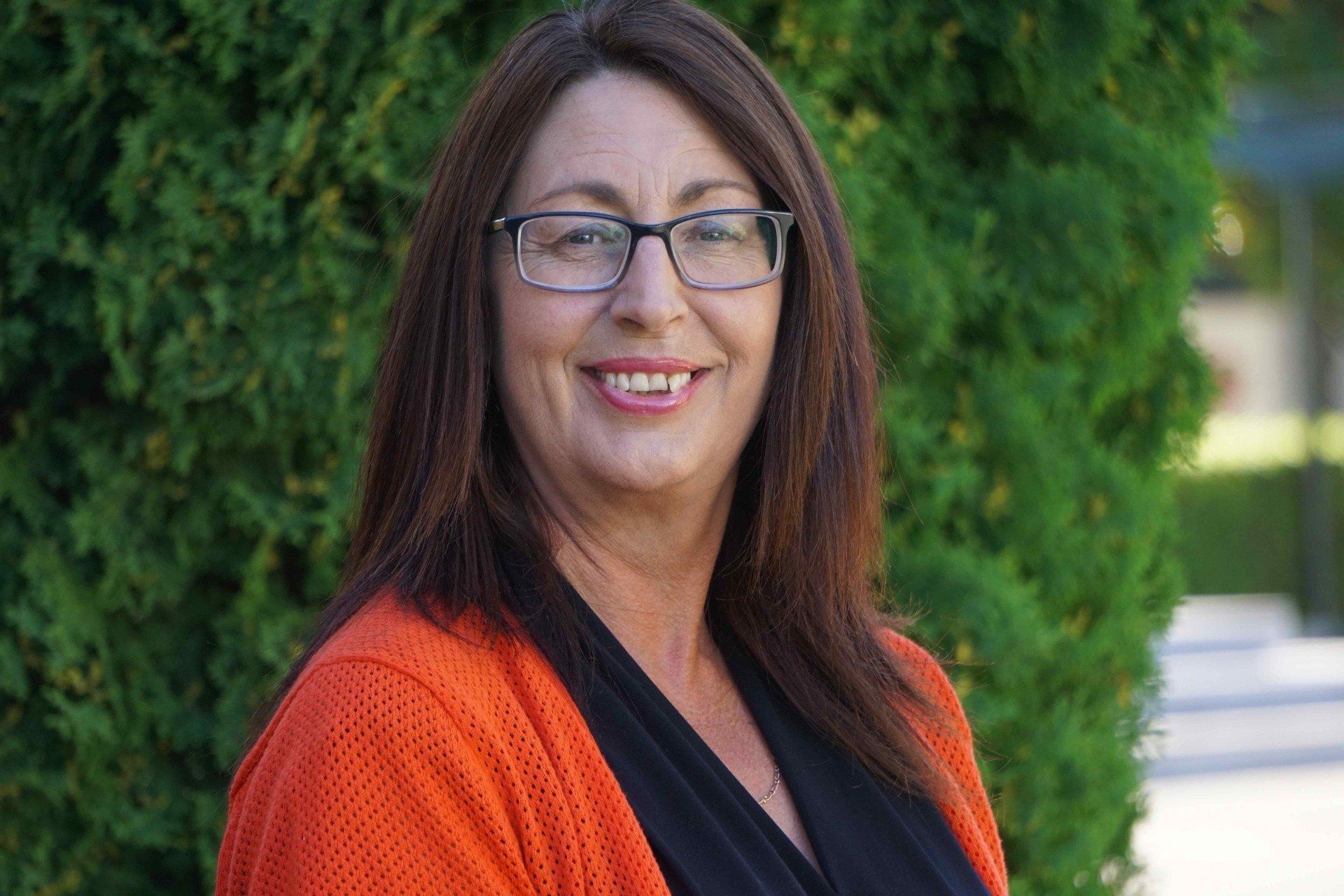 A woman wearing glasses and an orange sweater is smiling for the camera.