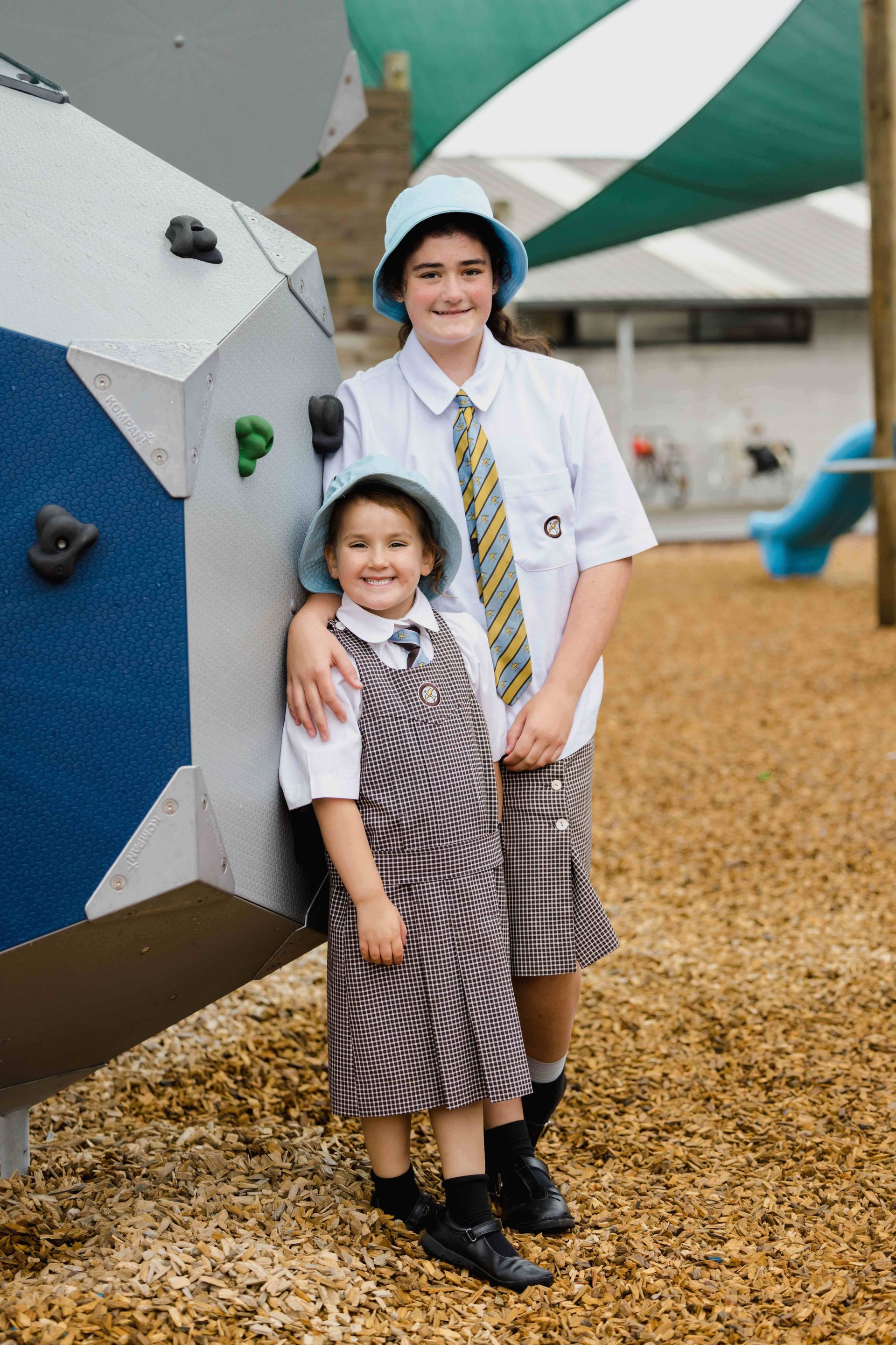 Two young girls in school uniforms are standing next to each other in a playground.