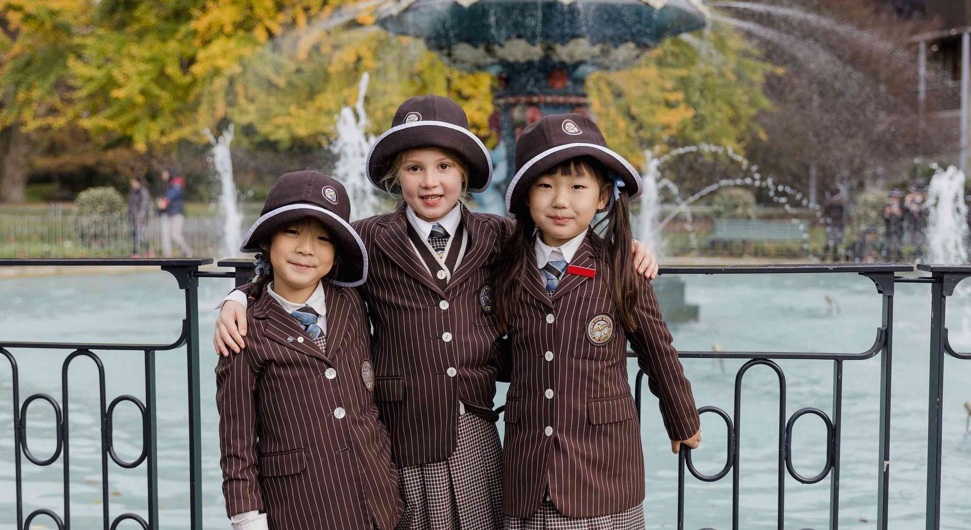 Three young boys are posing for a picture in front of a fountain.