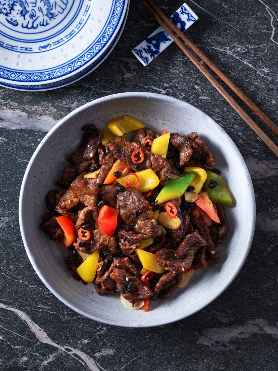 A bowl of beef and vegetables with chopsticks on a table.