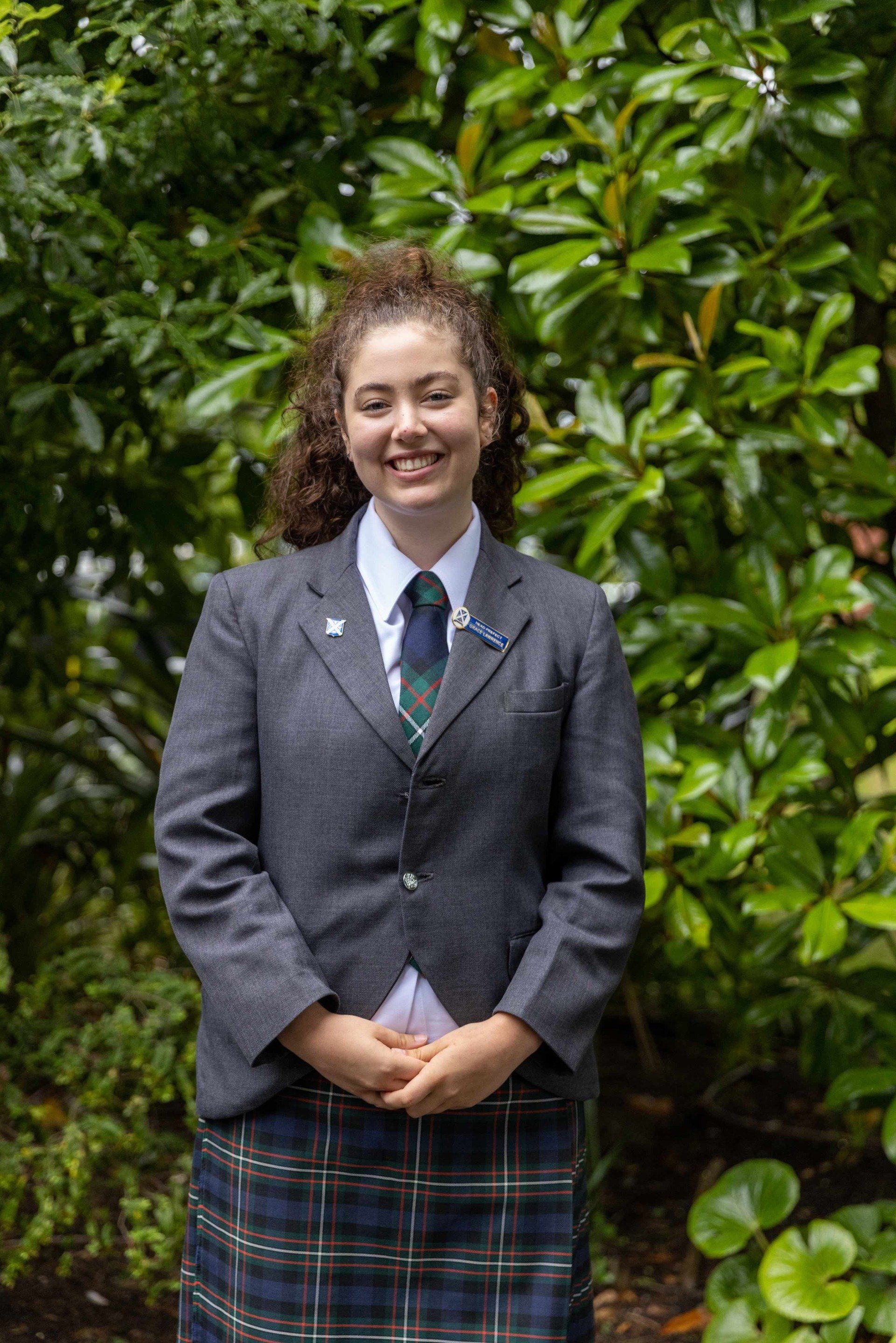 A young woman in a suit and tie is standing in front of a tree.