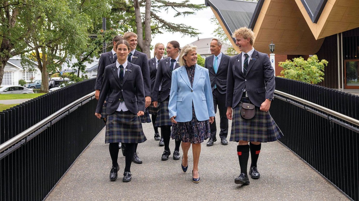 A group of people in kilts are walking across a bridge.