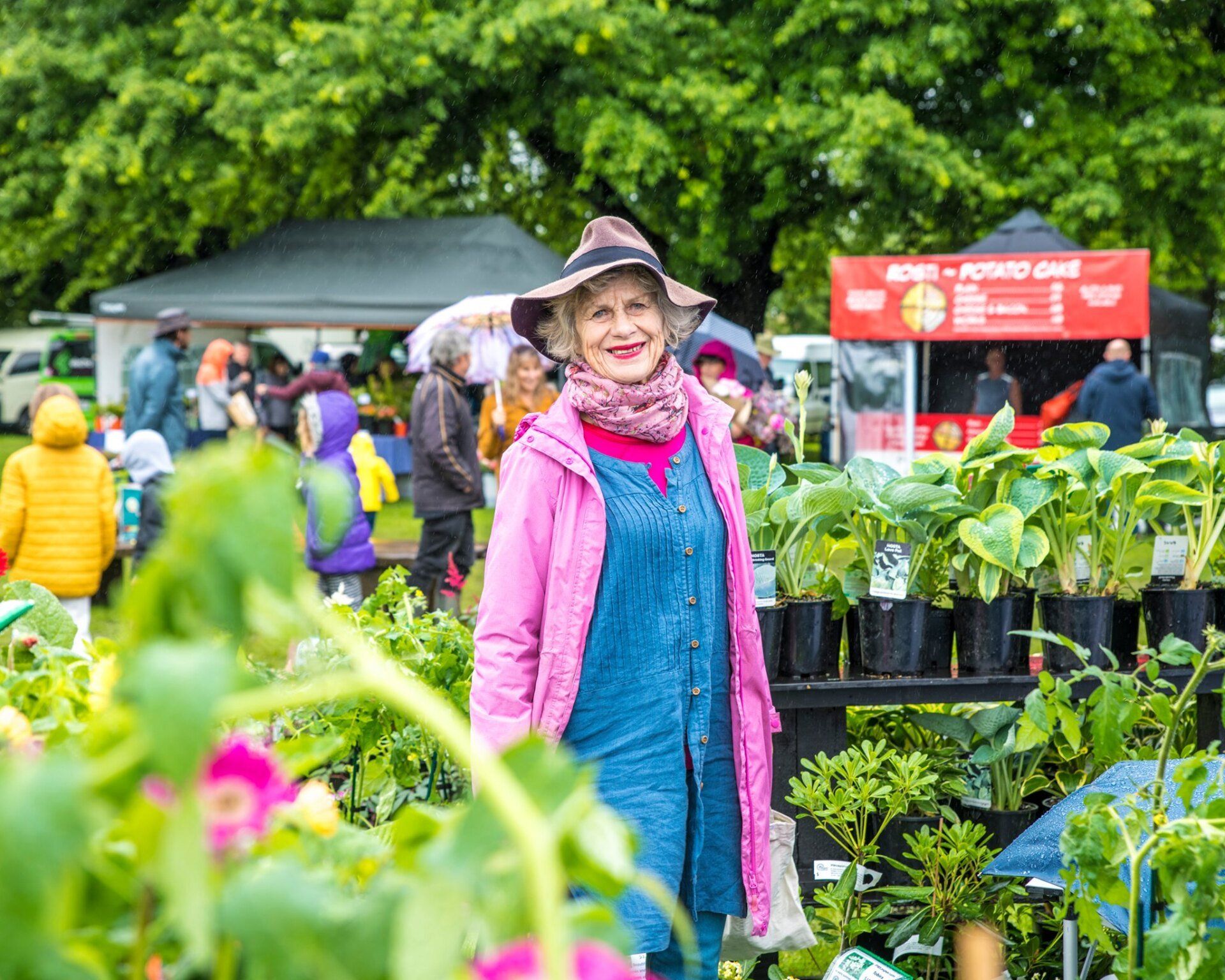 A woman is standing in front of a display of plants at a farmers market.