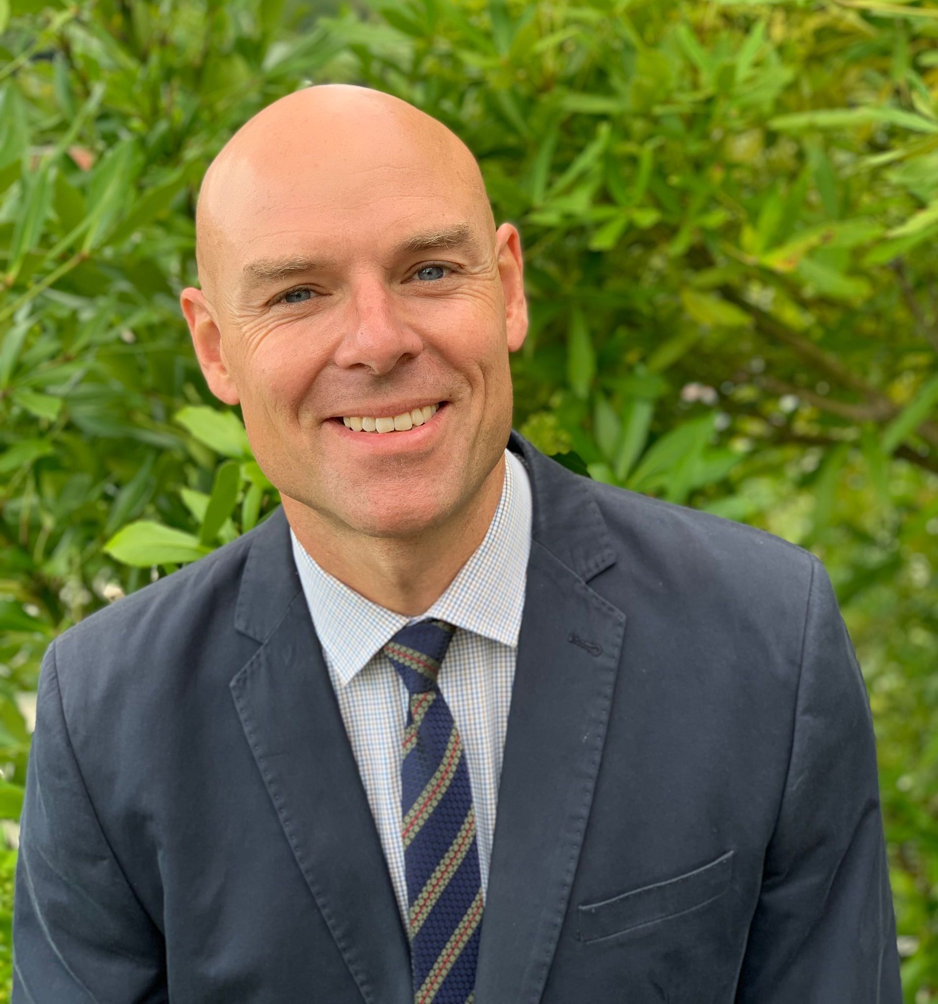 A bald man in a suit and tie is smiling for the camera.