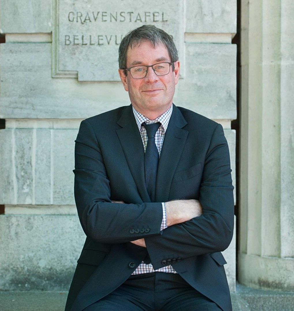 A man in a suit and tie is sitting with his arms crossed