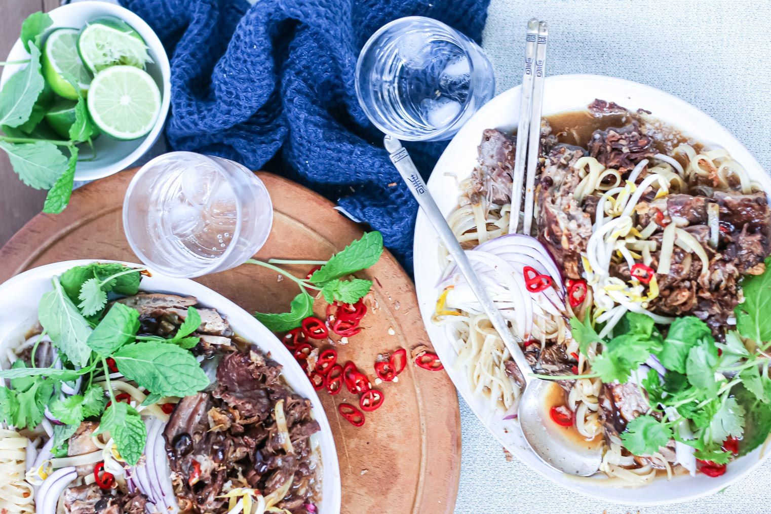 Two bowls of food with noodles , meat and vegetables on a table.