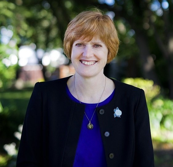 A woman wearing a blue shirt and a black jacket smiles for the camera