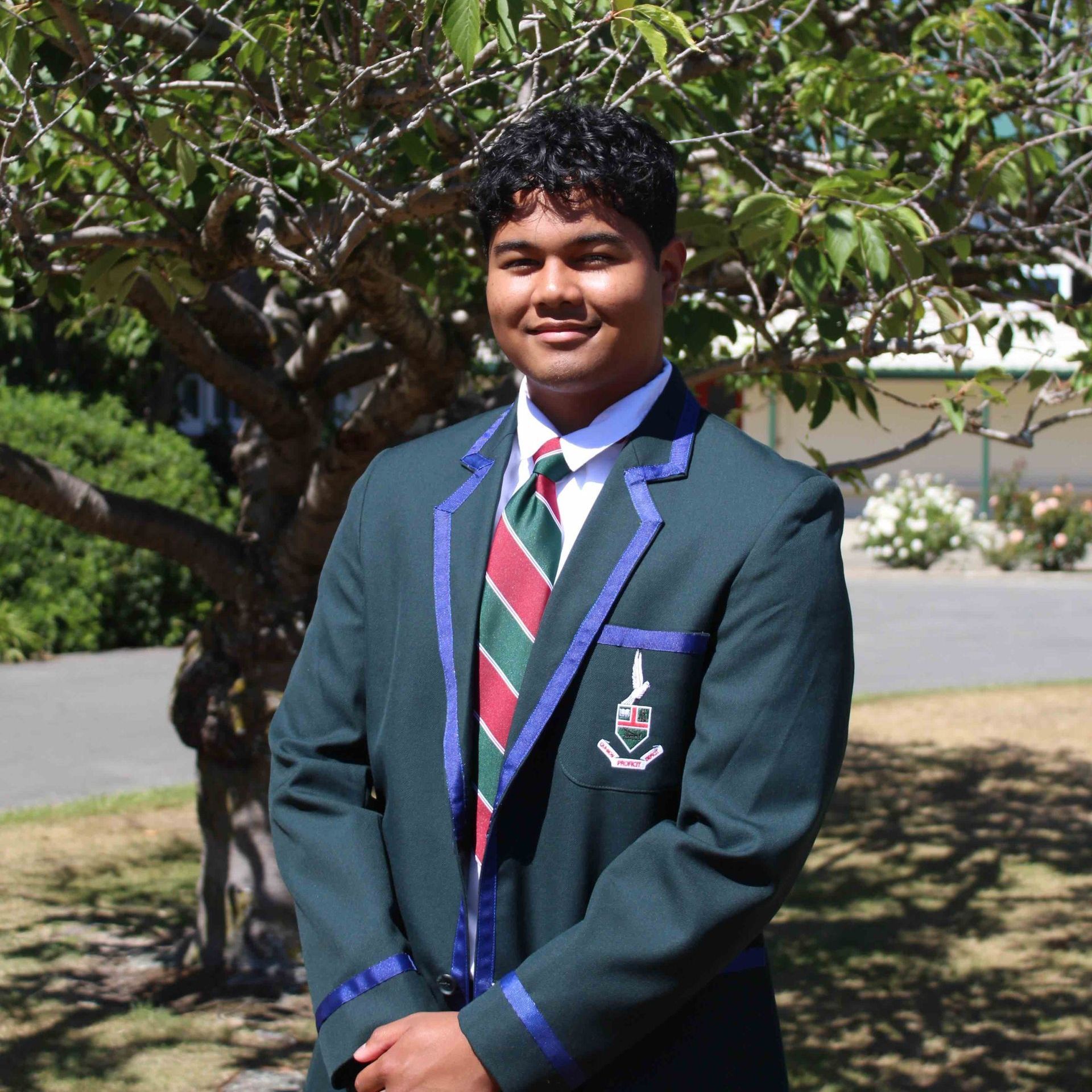 A young man in a suit and tie stands in front of a tree