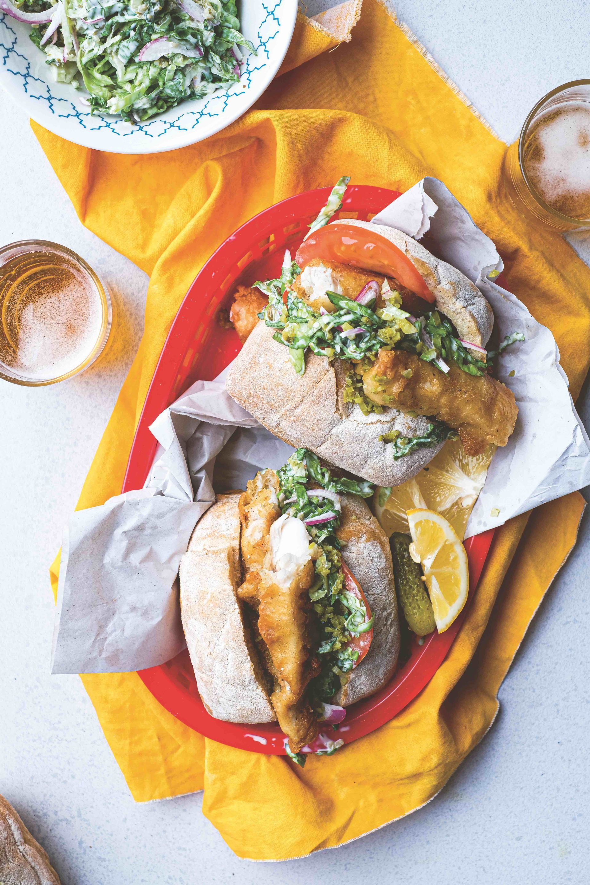 Two fish sandwiches are on a red plate on a yellow napkin.