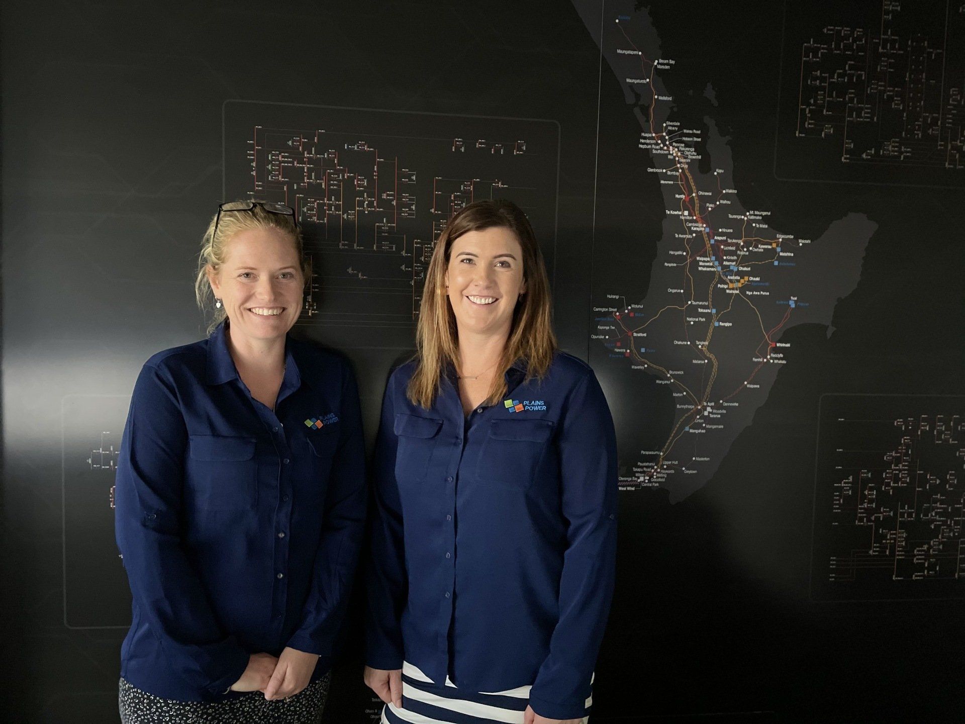 Two women are standing next to each other in front of a blackboard.