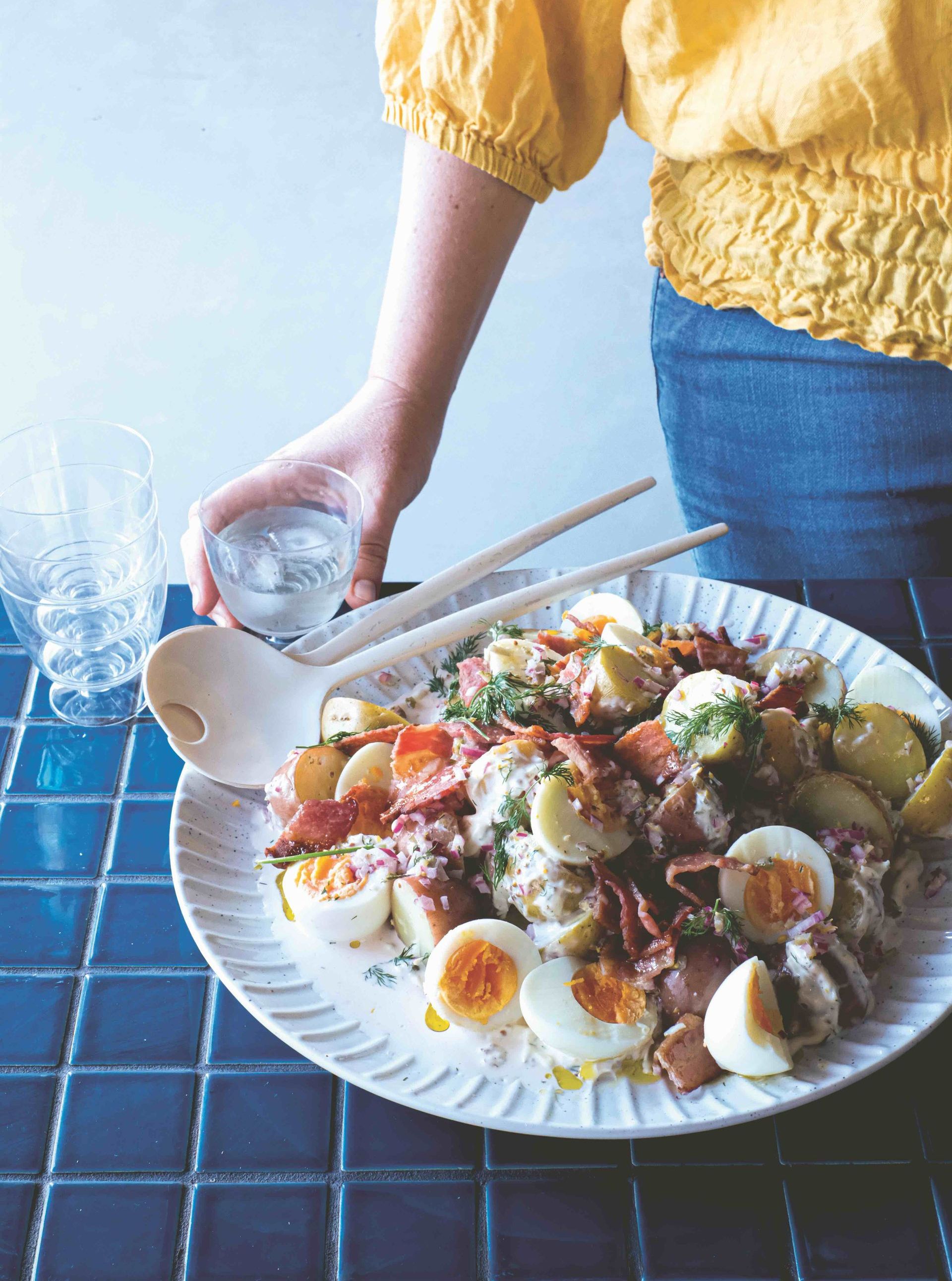 A person is holding a glass of water next to a plate of food.