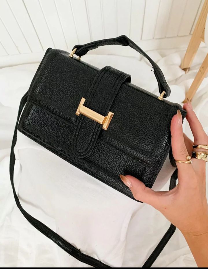 Una mujer sostiene un bolso negro con la letra h.