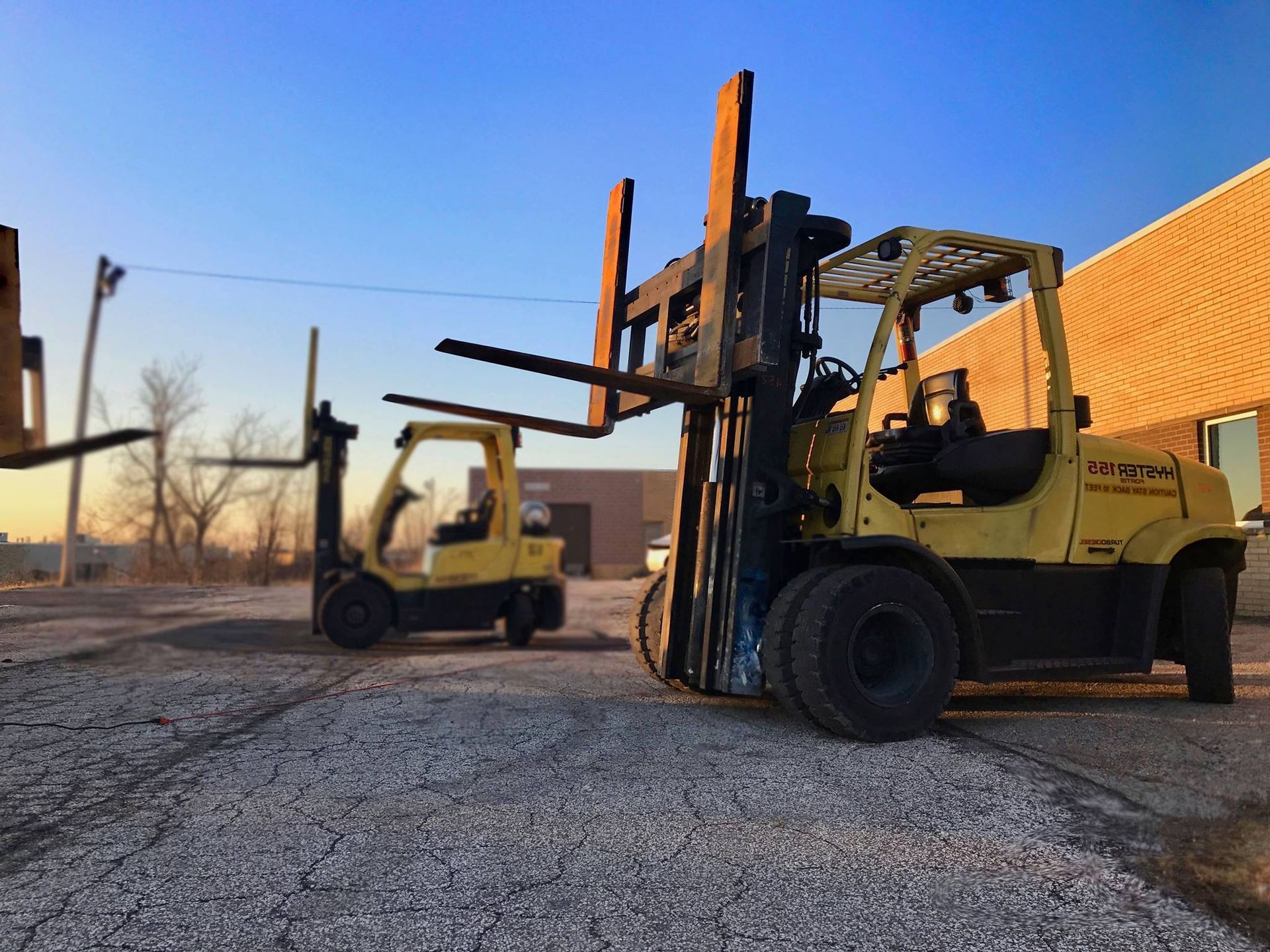 Yellow forklifts parked on gravel, a building in the background under a blue sky.