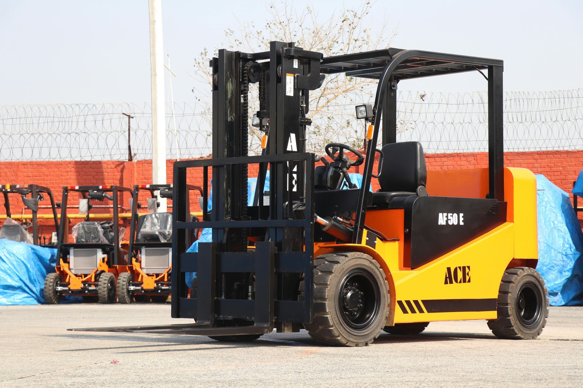 Yellow and black forklift on a paved lot with other equipment visible in the background.