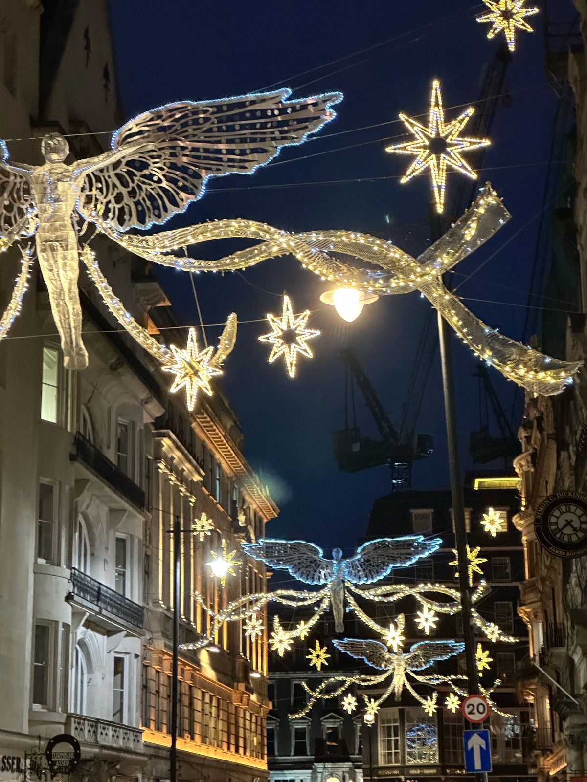 Christmas decorations with angel and star lights in a city street at dusk.
