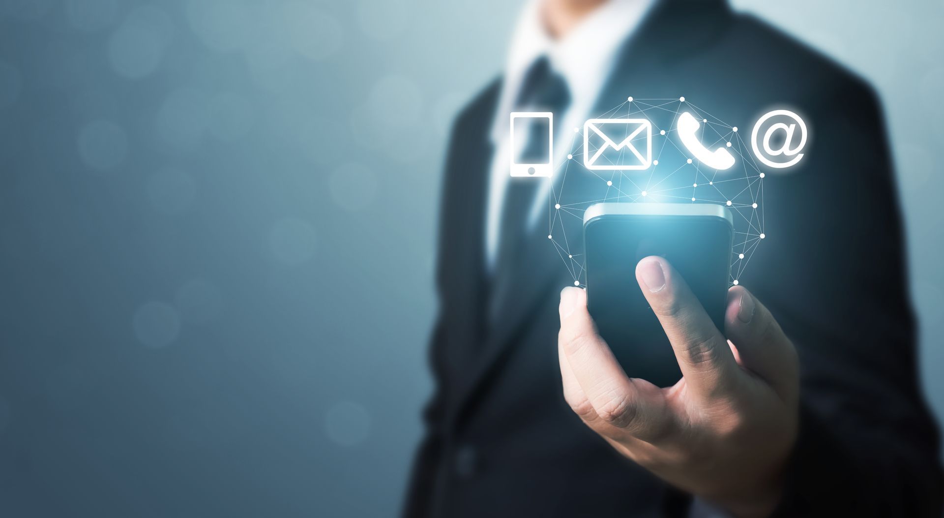 A man in a suit is holding a cell phone with contact icons coming out of it.