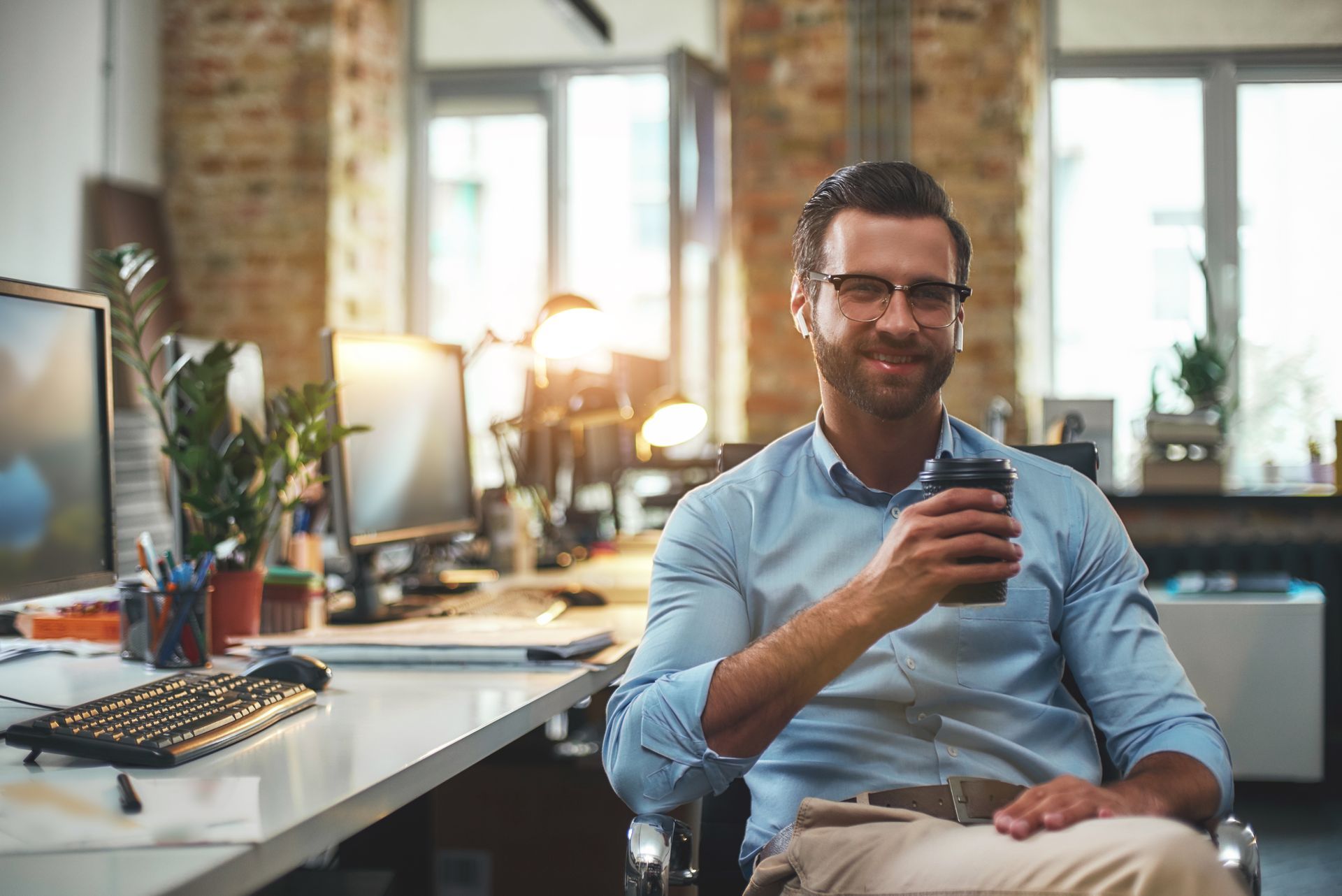 A man is sitting at a desk in an office holding a cup of coffee.