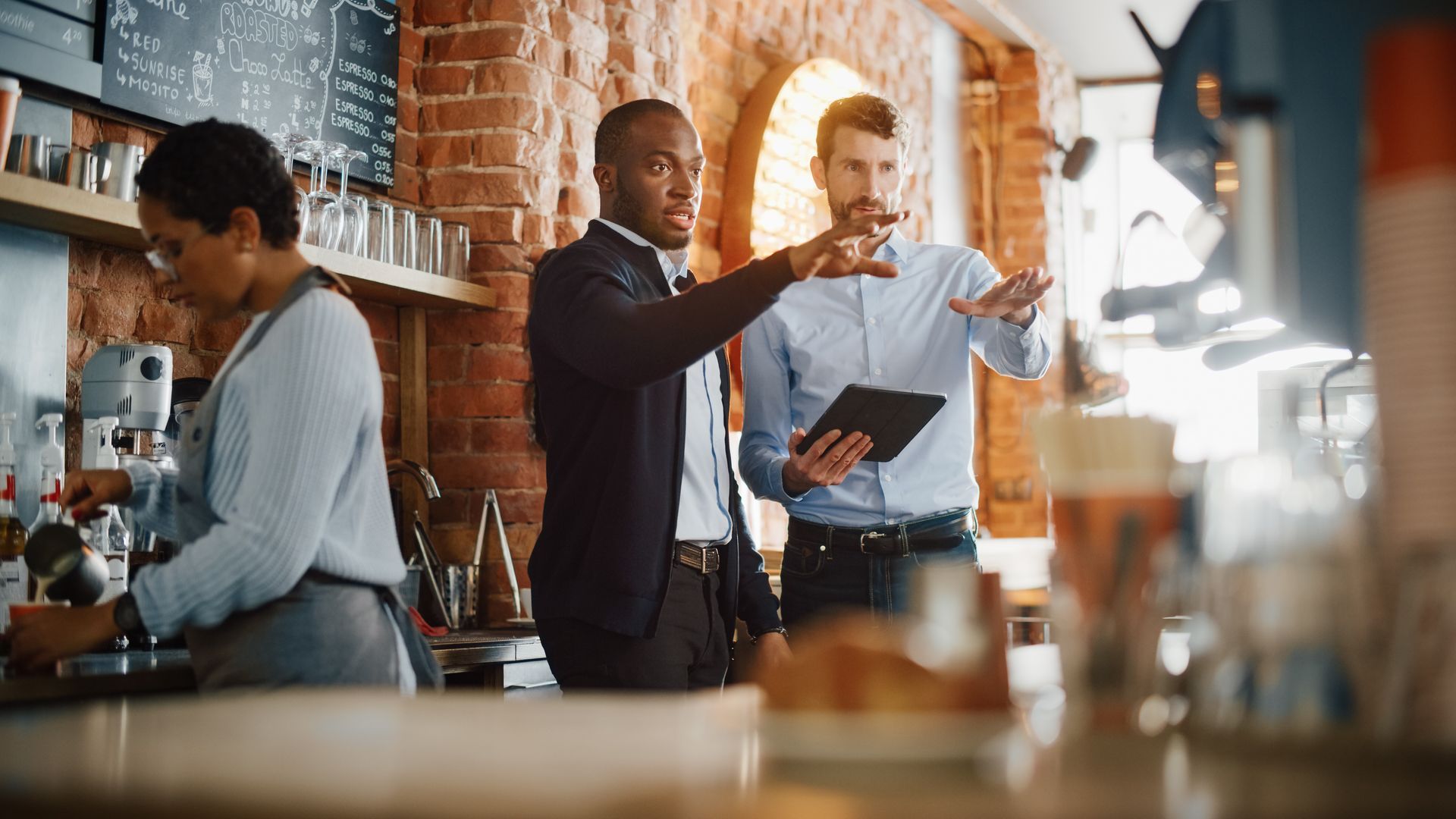A group of people are standing in a restaurant looking at a tablet.