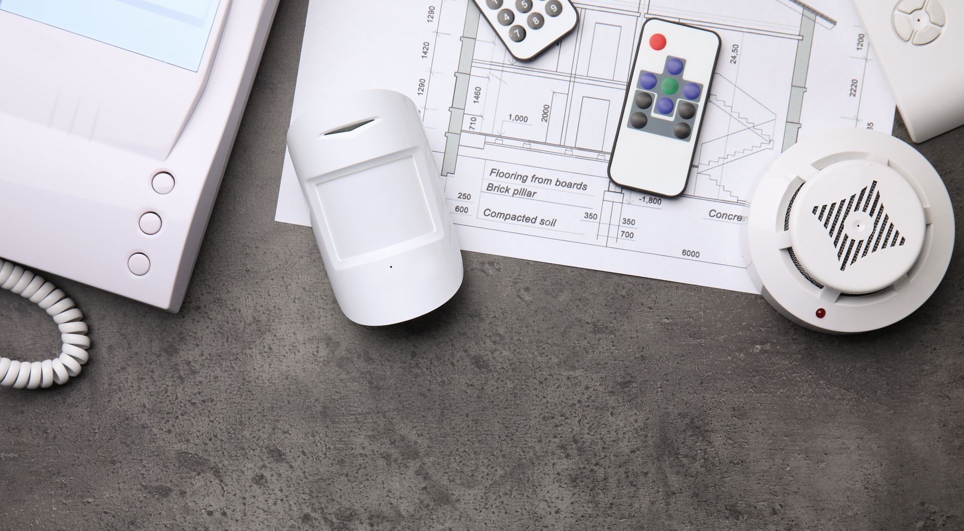A security system is sitting on a table next to a smoke detector and a remote control.