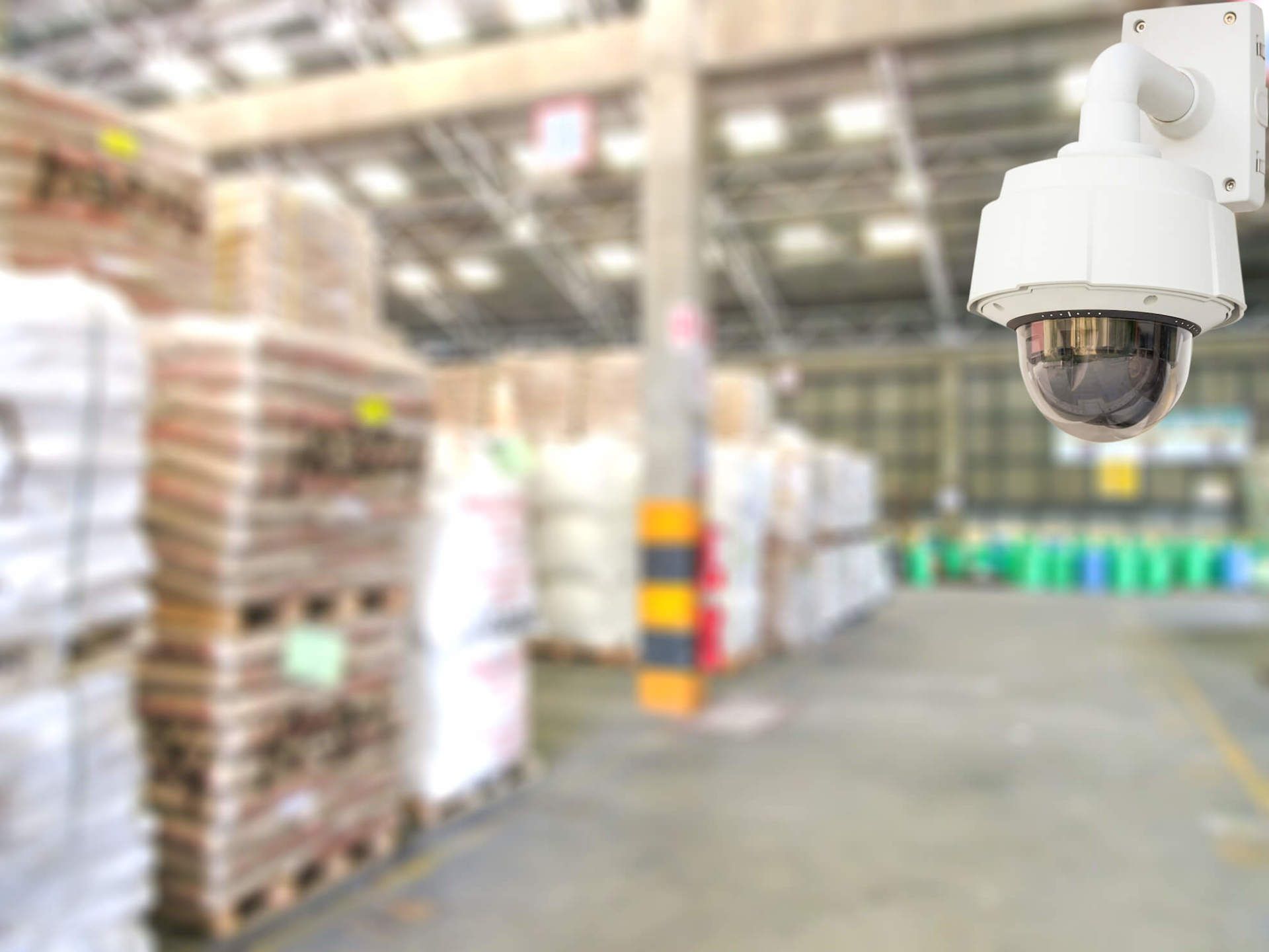 A security camera is hanging from the ceiling of a warehouse.