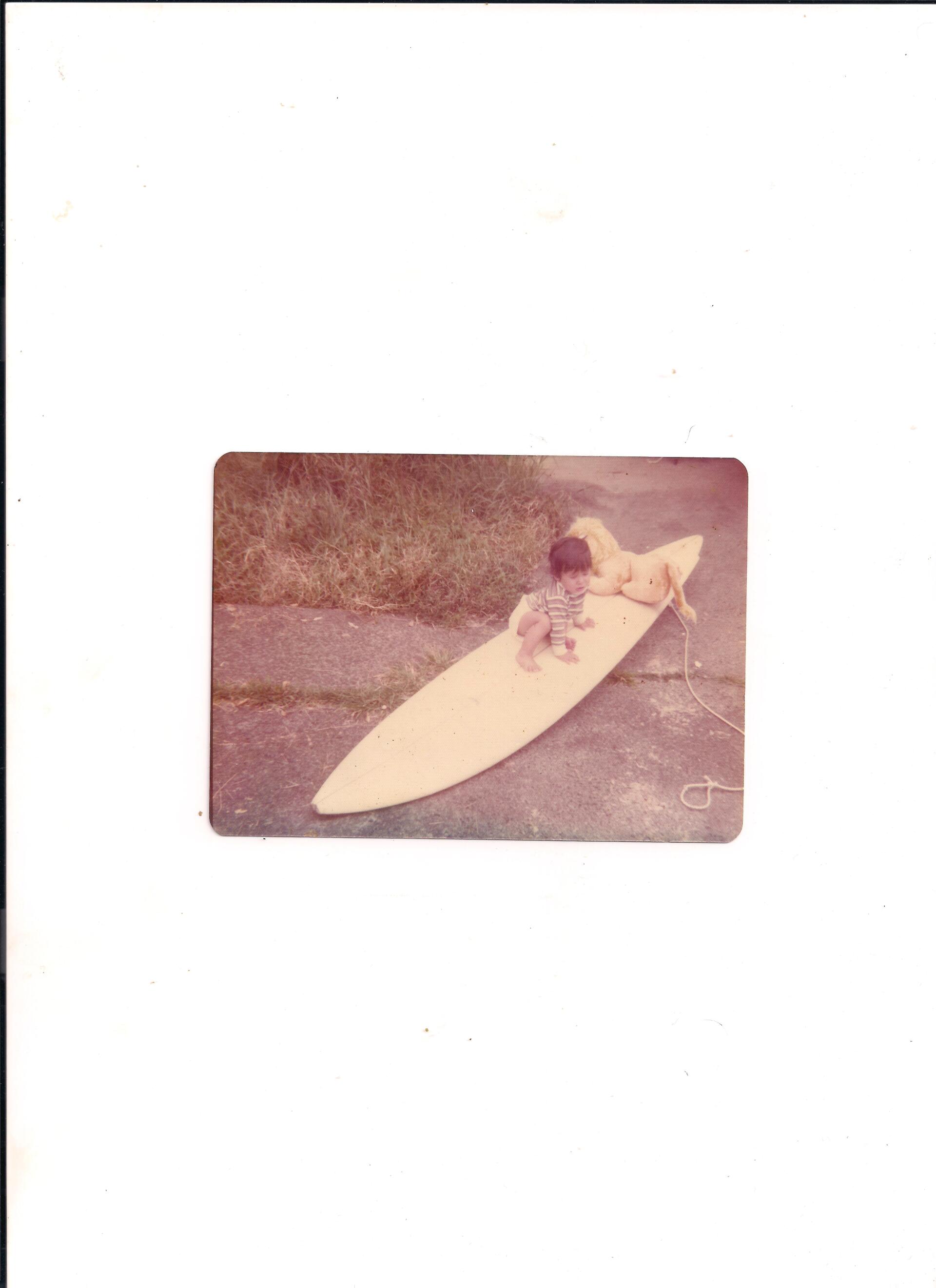 A child is sitting on a surfboard on the sidewalk.