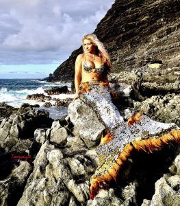 A woman in a mermaid costume is sitting on a rock near the ocean.