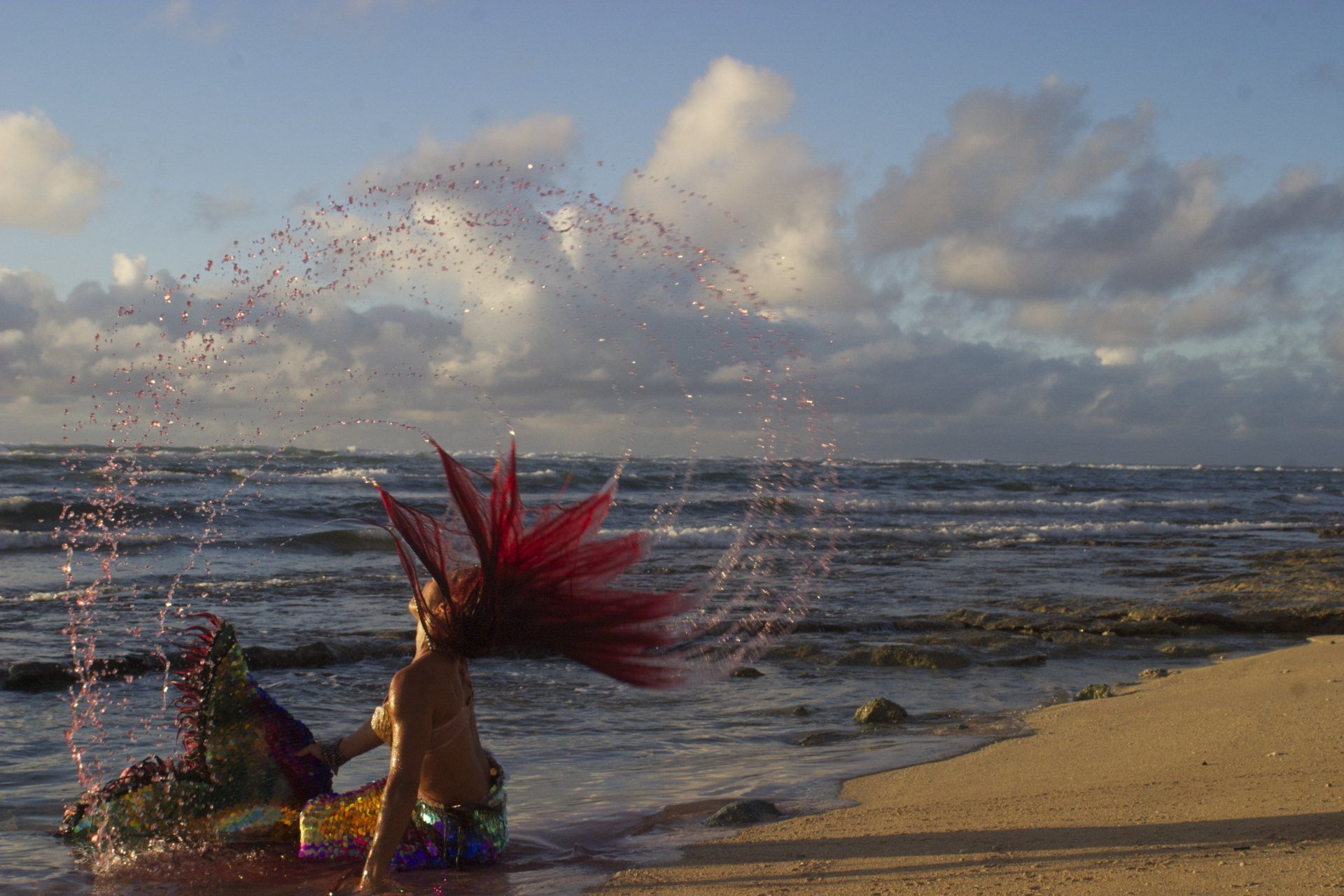 A woman with red hair is splashing water on the beach