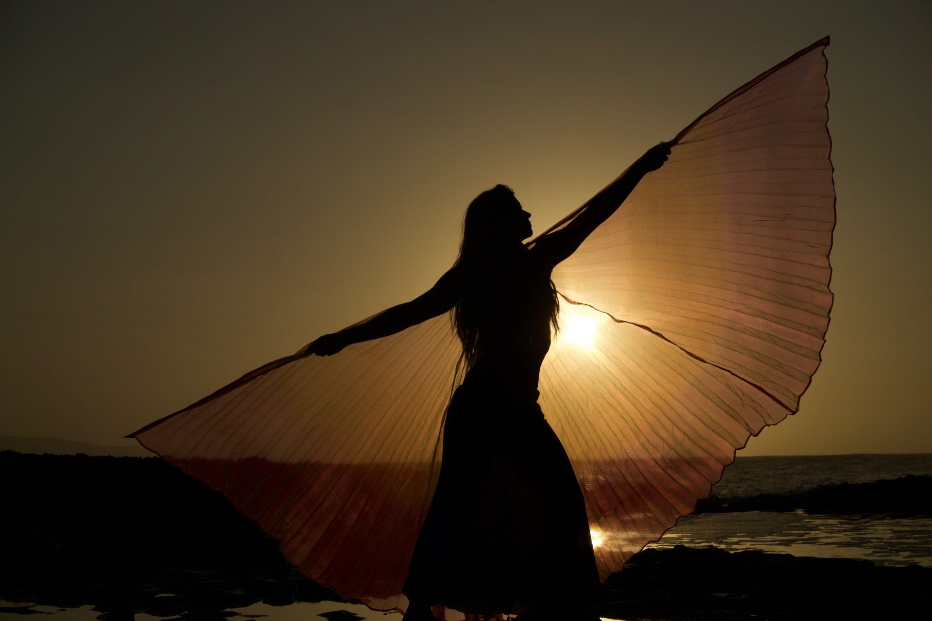 A silhouette of a woman standing on the beach with her arms outstretched