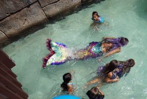 A group of children are swimming in a pool with a mermaid.