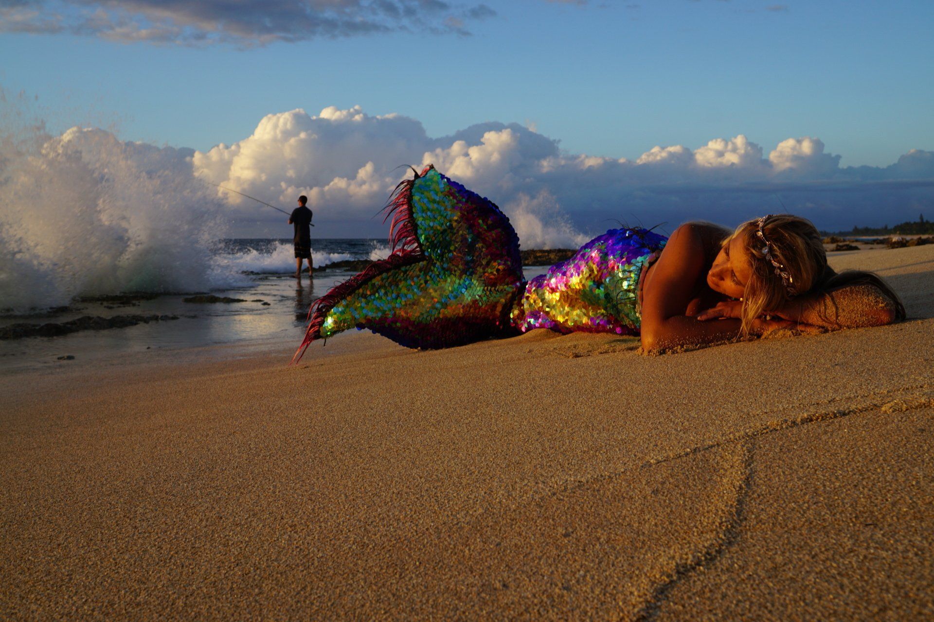 A woman in a mermaid costume is laying on the beach.