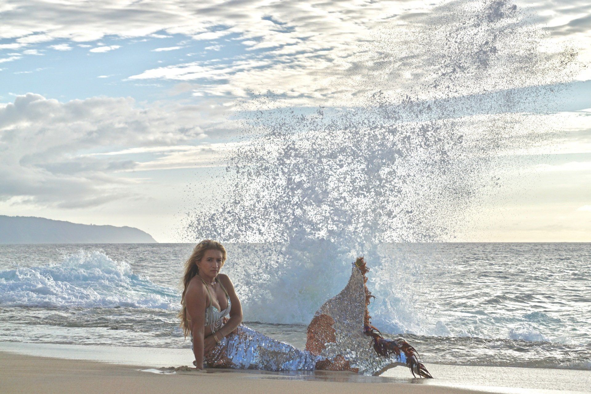 A woman in a mermaid costume is laying on the beach.