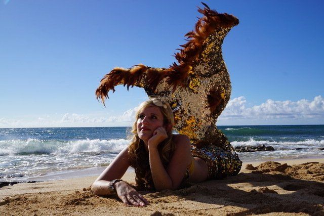 A woman in a mermaid costume is laying on the beach.