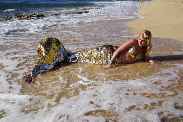 A woman in a mermaid costume is laying on the beach.