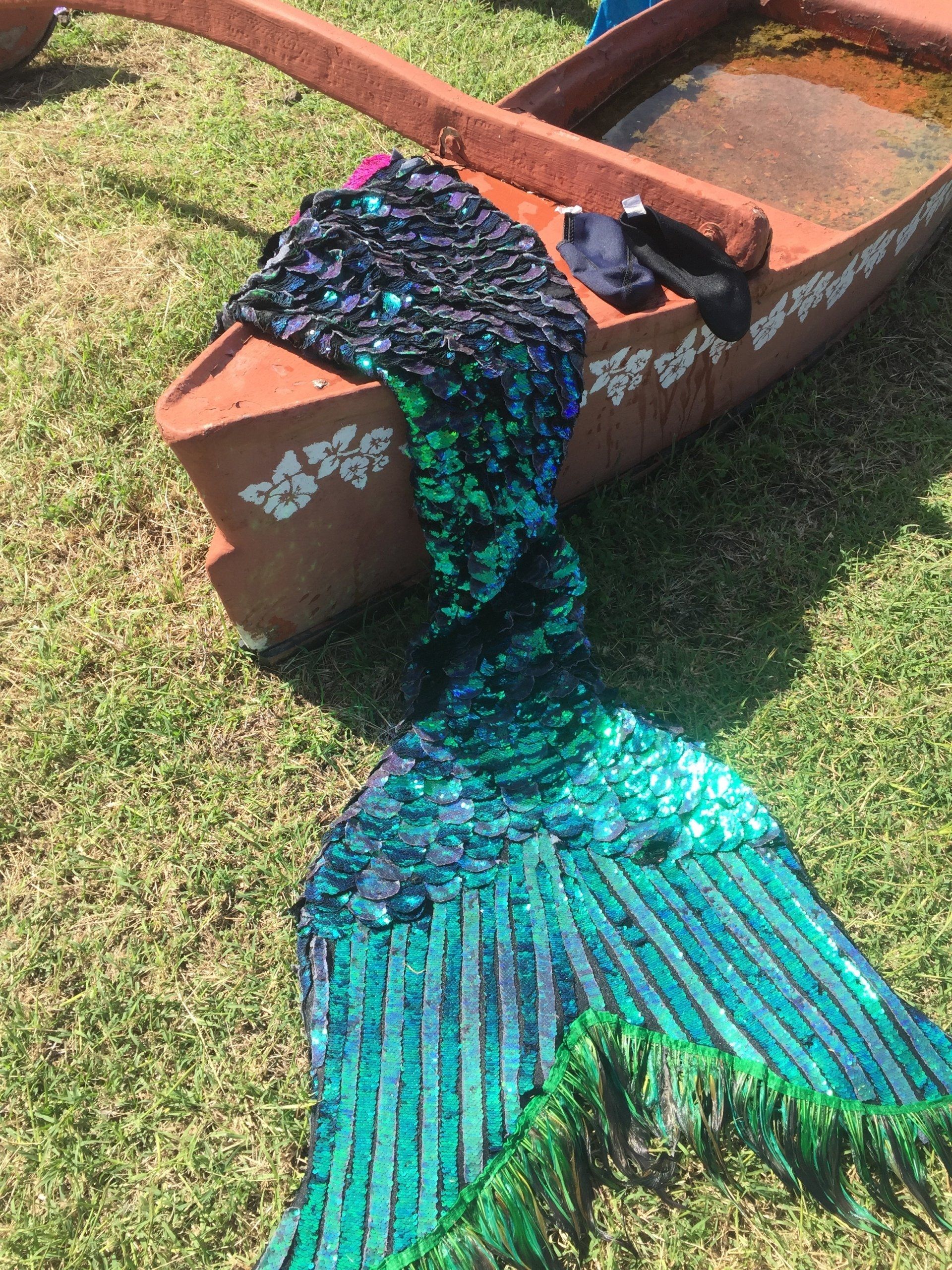 A mermaid tail is laying on the grass next to a boat
