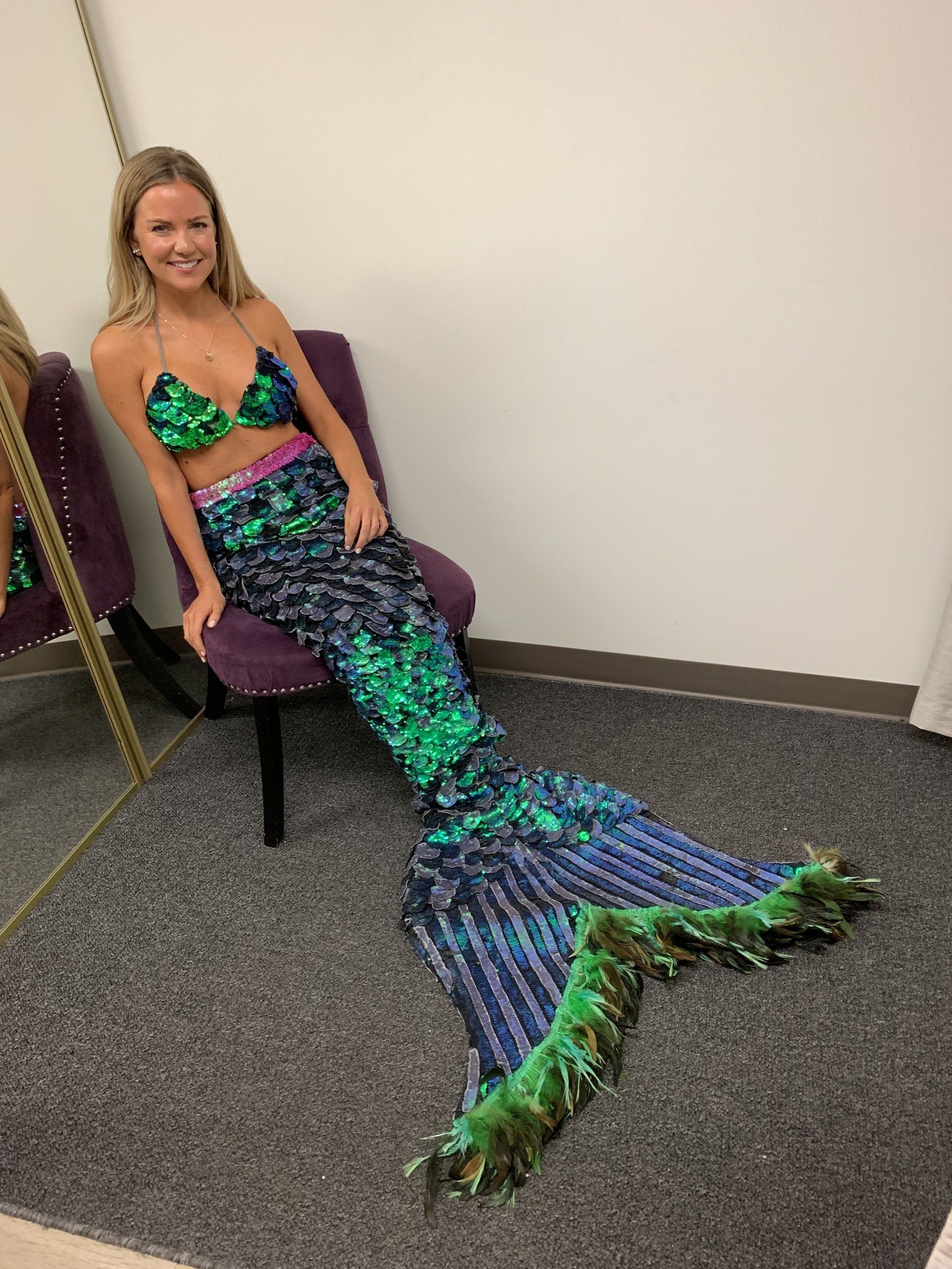 A woman in a mermaid costume is sitting in a chair in front of a mirror.