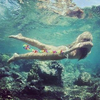 A woman is swimming underwater with a lei around her neck.