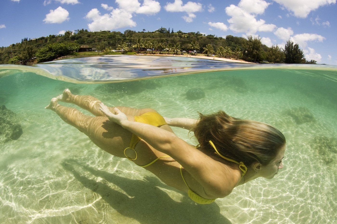 A woman in a yellow bikini is swimming underwater in the ocean.