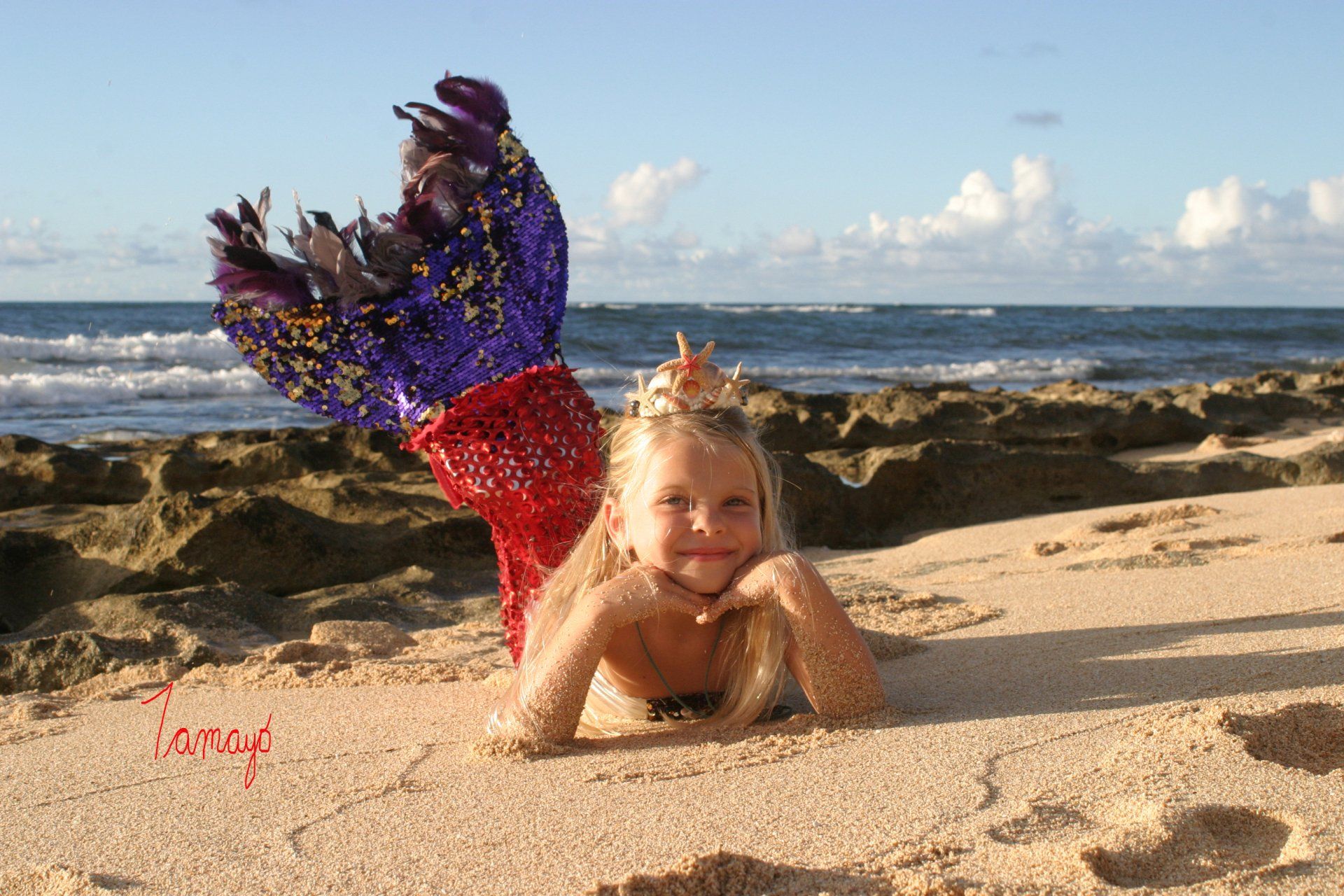 A little girl in a mermaid costume is laying on the beach