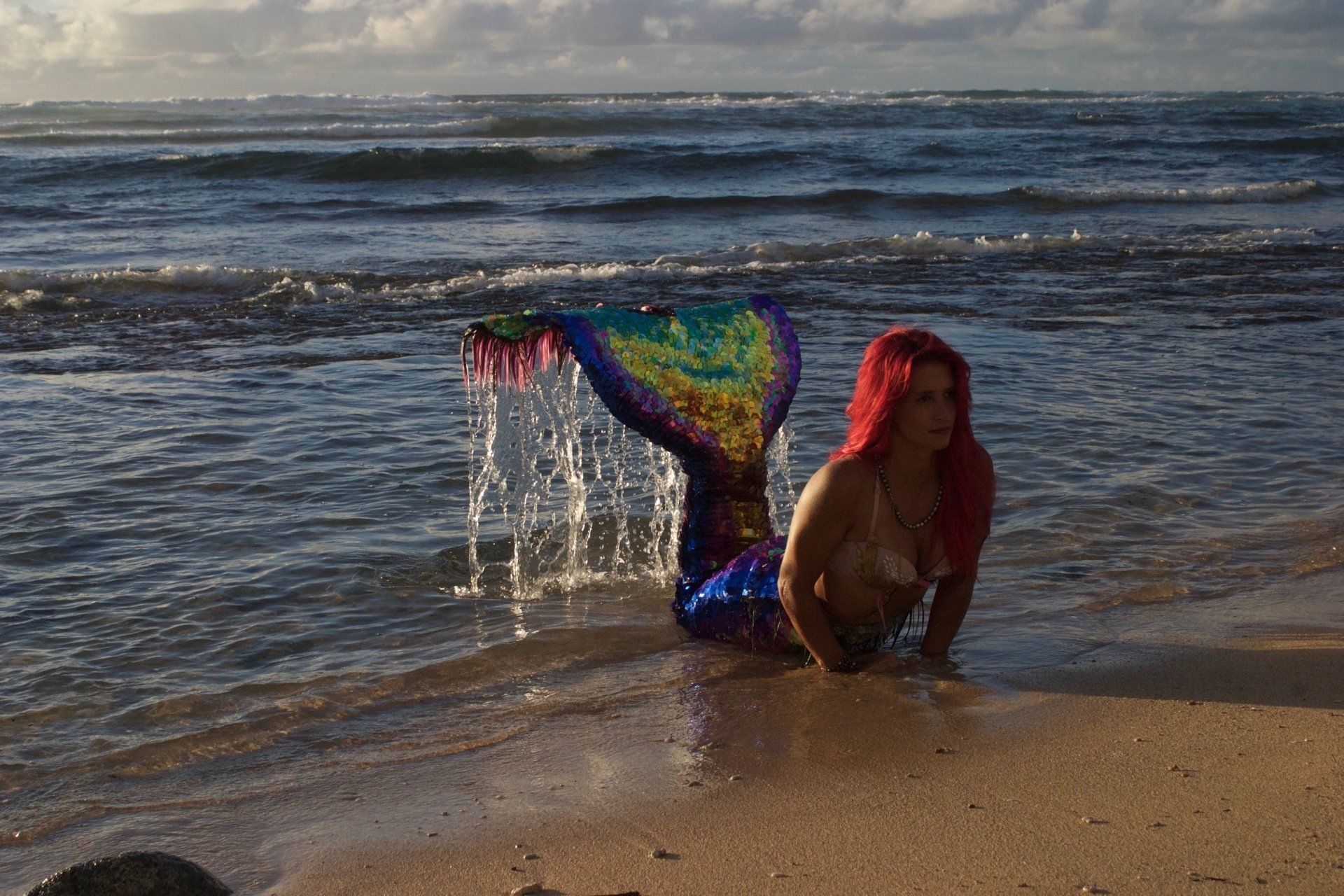 A woman in a mermaid costume is laying on the beach.