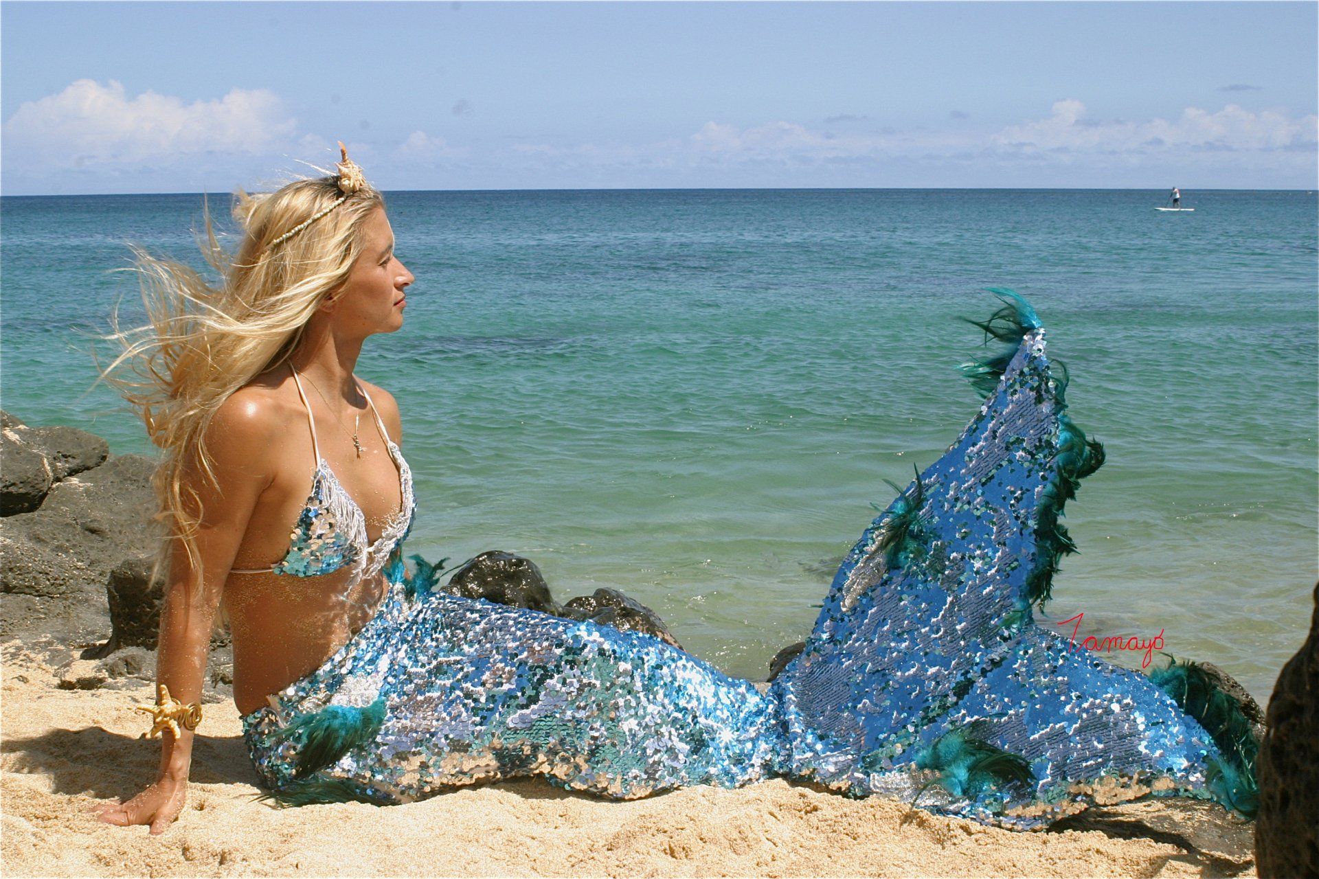 A woman in a mermaid costume is sitting on the beach