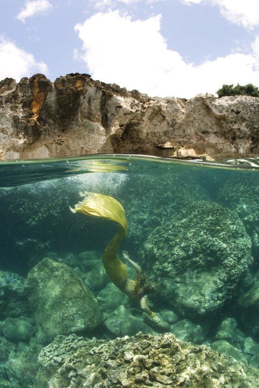 A half underwater photo of a mermaid swimming in the ocean