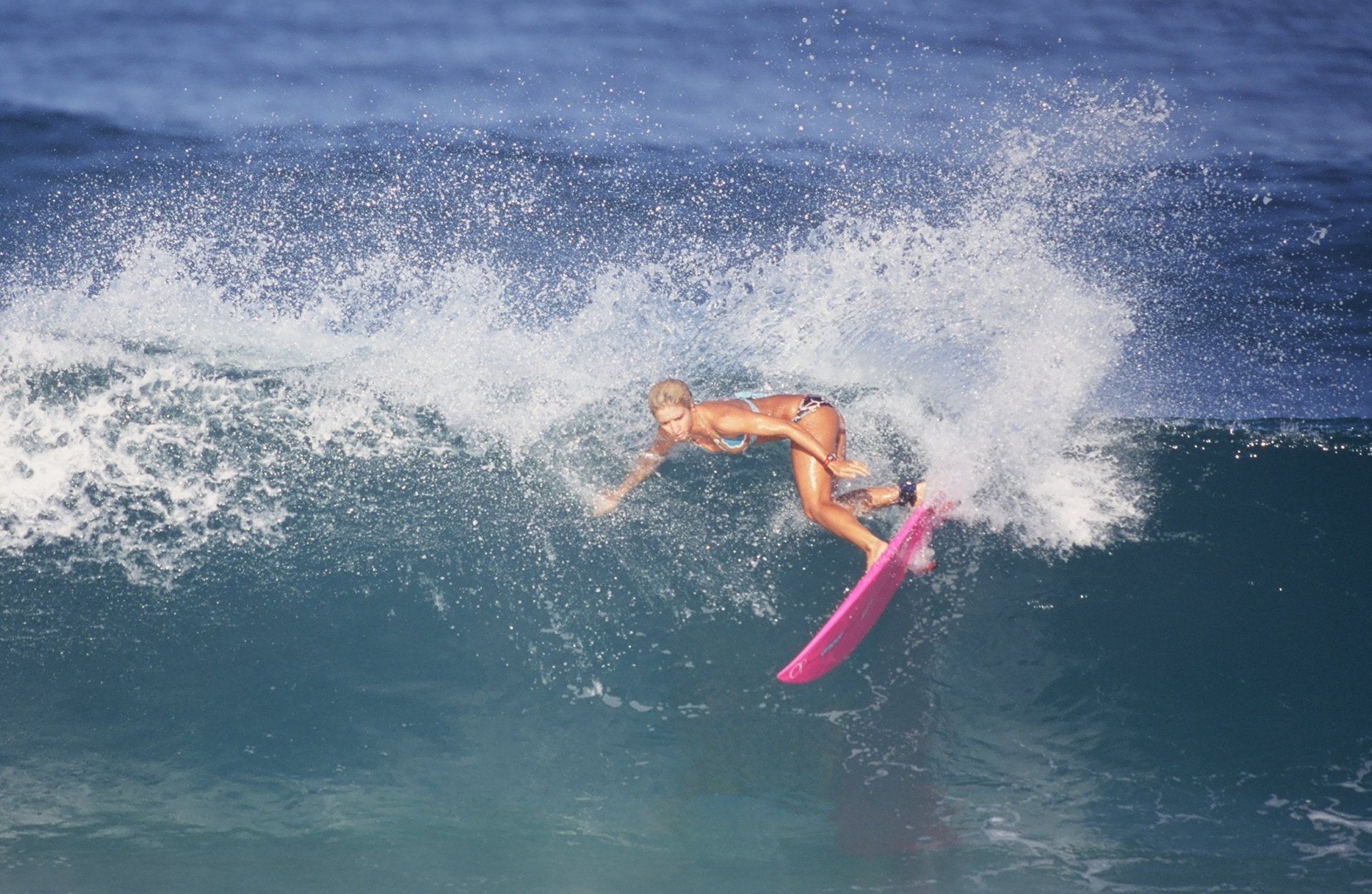 A woman is riding a wave on a pink surfboard