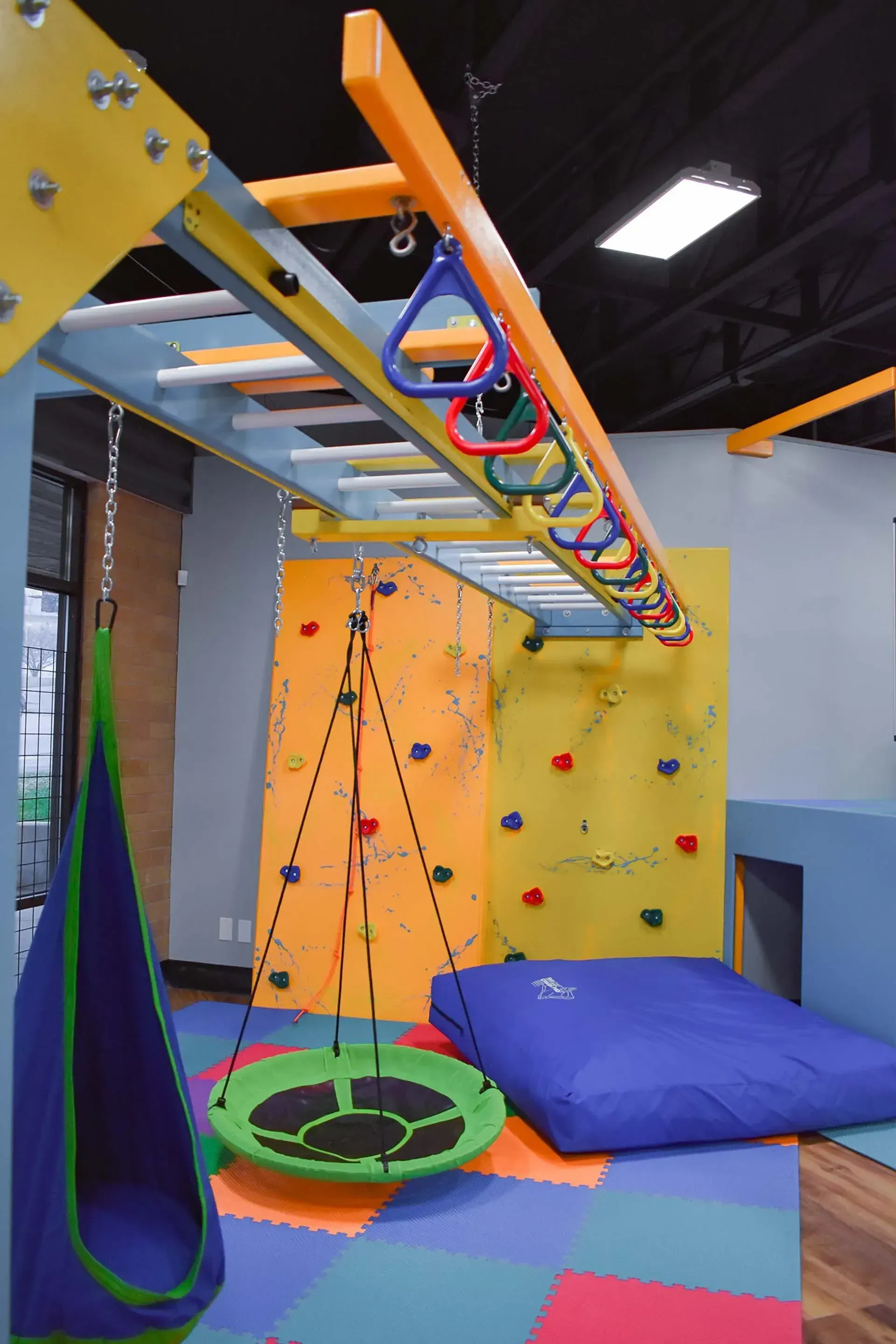 Playroom with climbing wall, monkey bars, swing, and floor mats.
