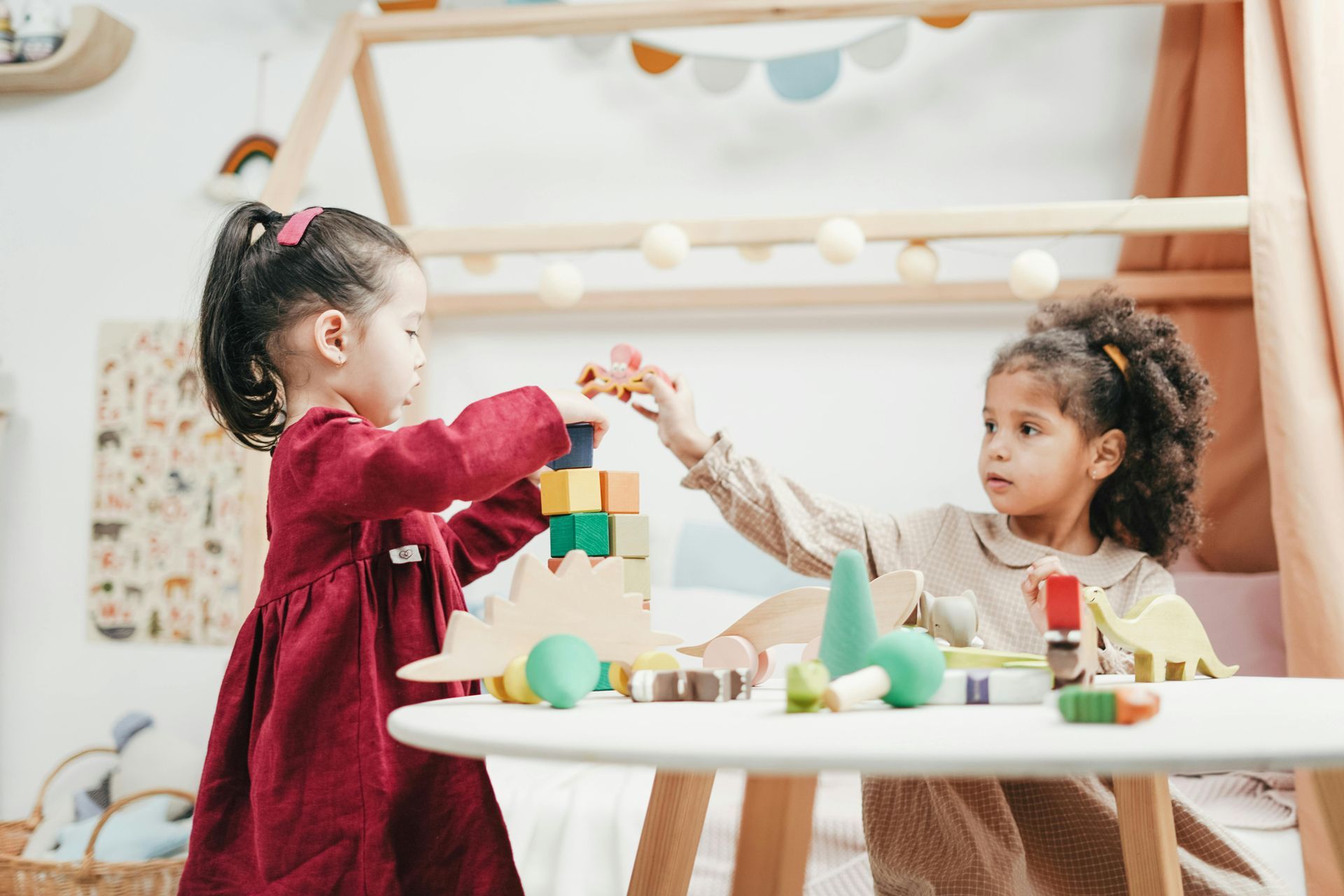 Two children building a tower with colorful wooden blocks on a white table in a playroom.