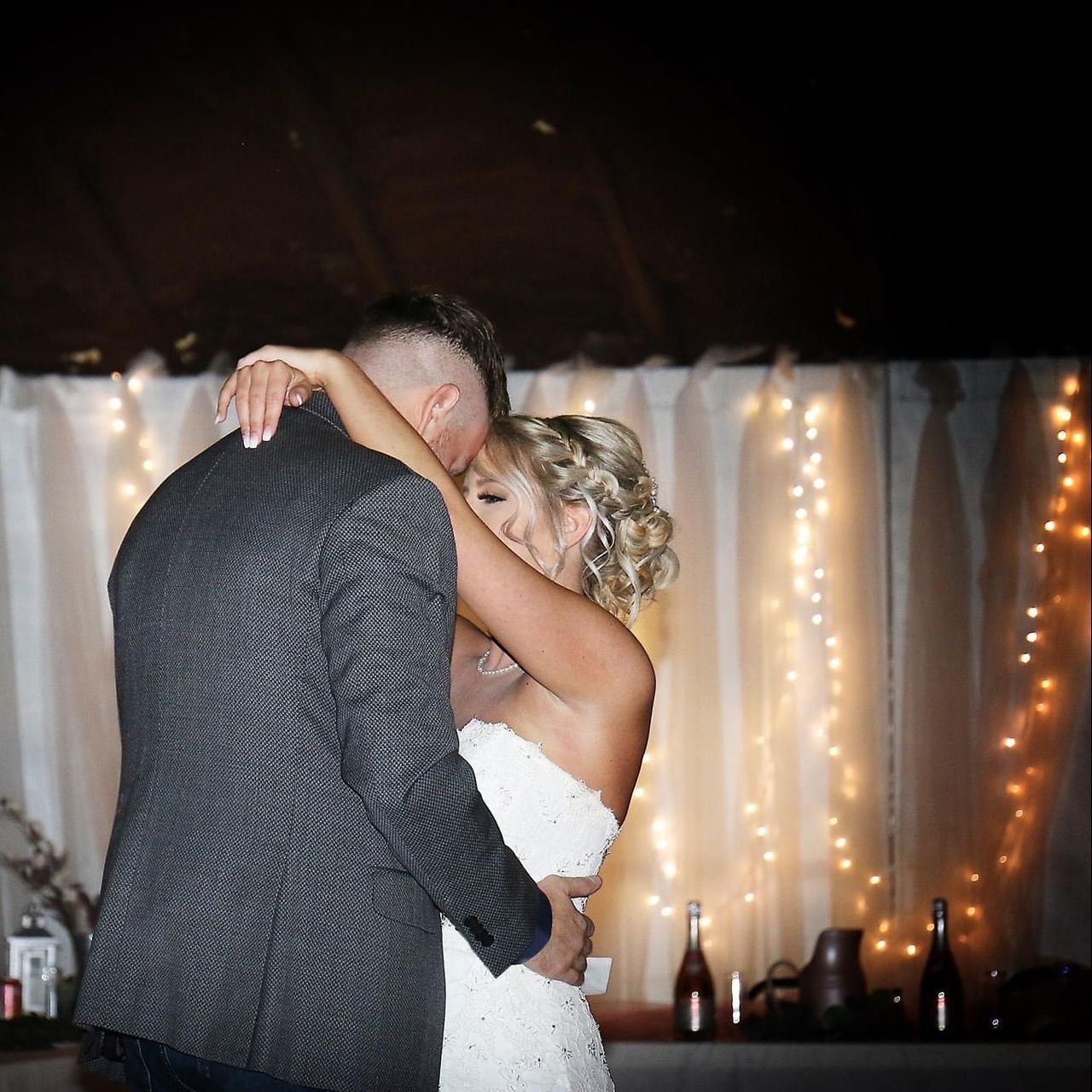 a bride and groom are dancing in front of a string of lights