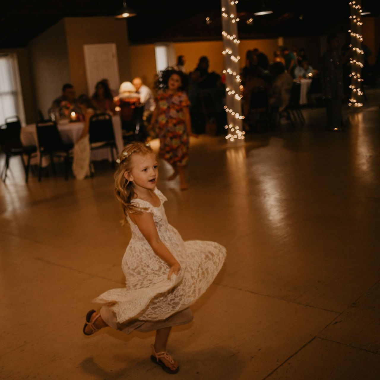a little girl in a white dress is dancing on a dance floor at a wedding reception .