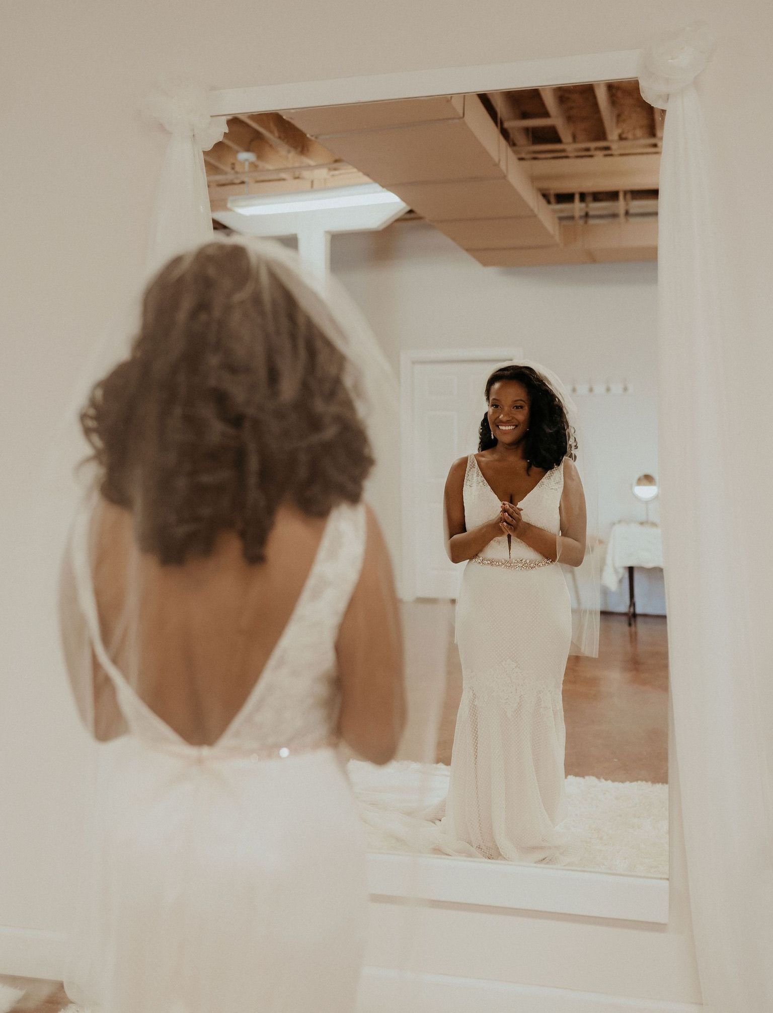a woman in a wedding dress is standing in front of a mirror smiling.