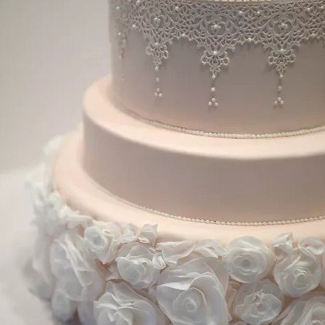 a close up of a wedding cake with white roses and lace .
